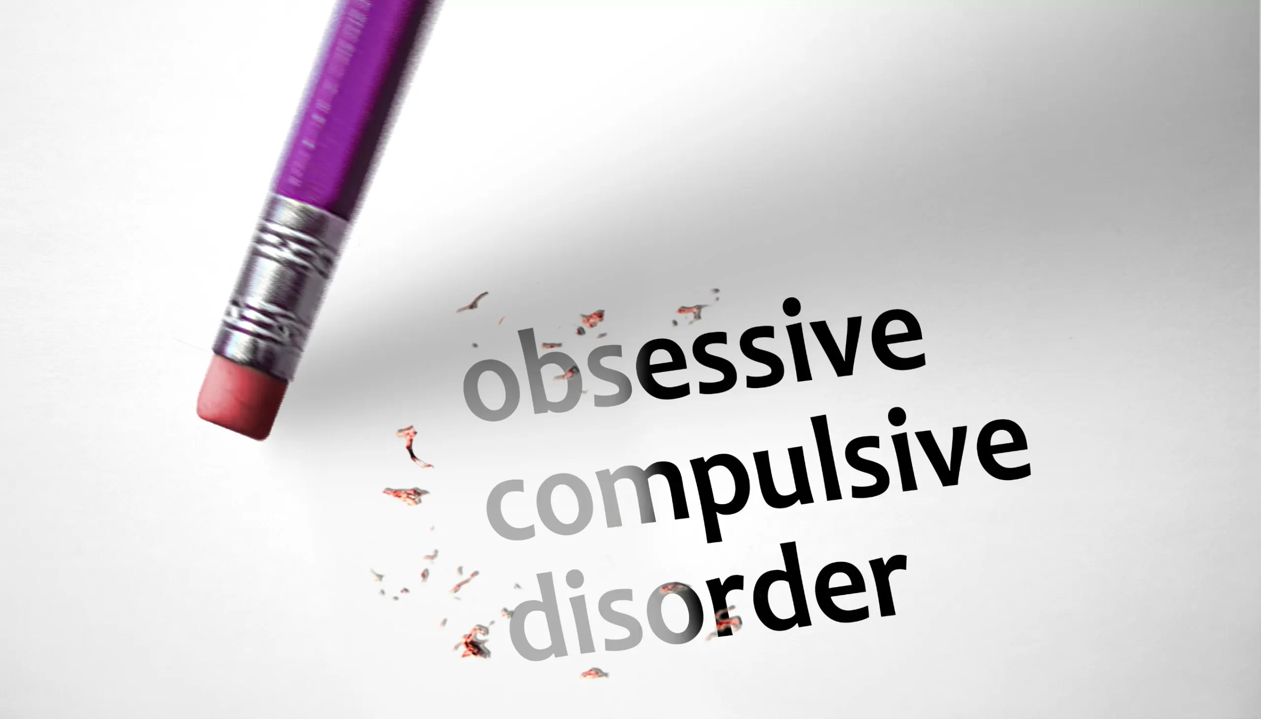 A pencil eraser is partially erasing the words "obsessive compulsive disorder" on a white surface, symbolizing the idea of change and raising awareness during OCD Week.