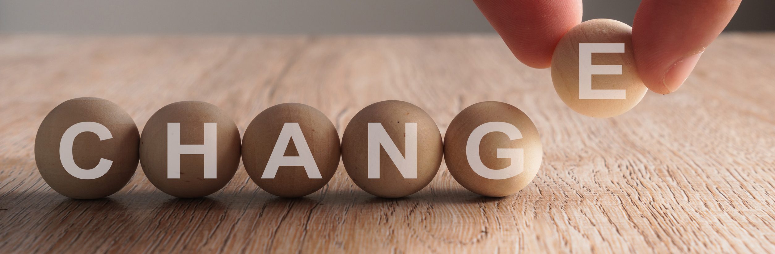 A hand confidently replaces the letter "G" with "E" in a row of wooden spheres spelling "CHANGE," serving as a subtle reminder of how to navigate life's changes with grace and adaptability.