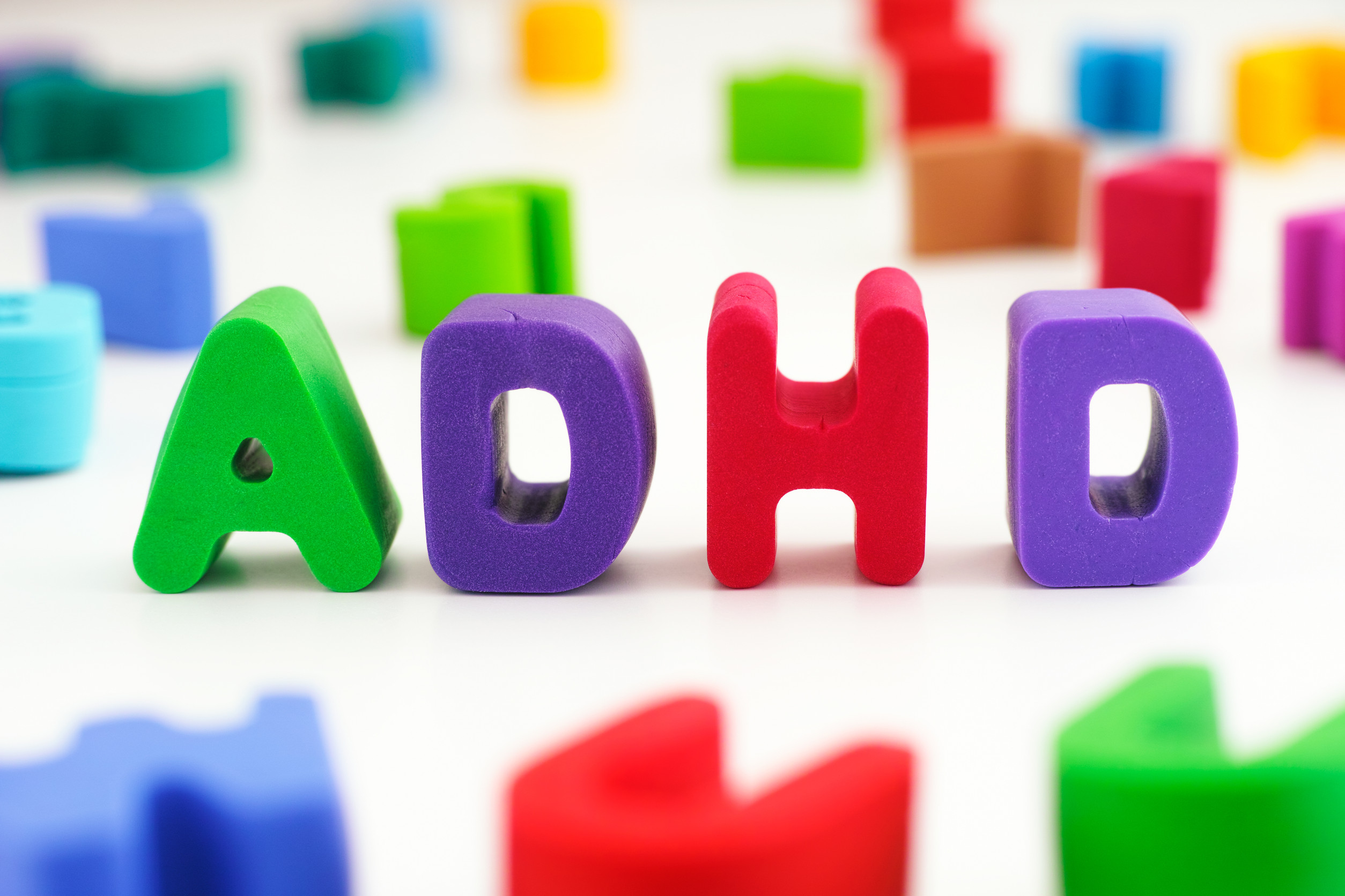 Colorful foam letters spelling “ADHD” are arranged in the center, with other scattered letters and shapes blurred in the background, symbolizing the variety of ADHD treatment options available in Minnesota.