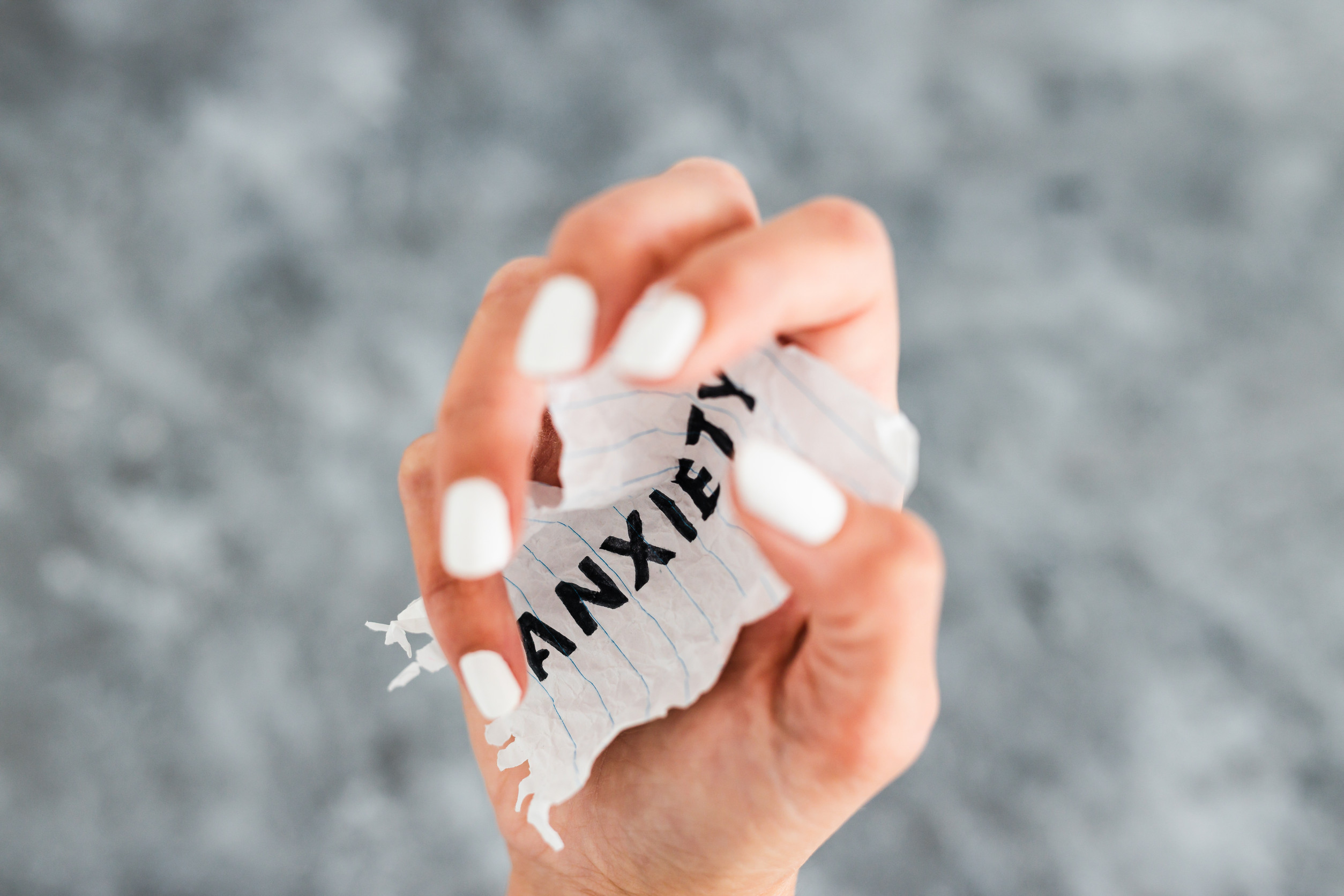 A hand with white painted nails tightly squeezes a crumpled piece of lined paper with the word