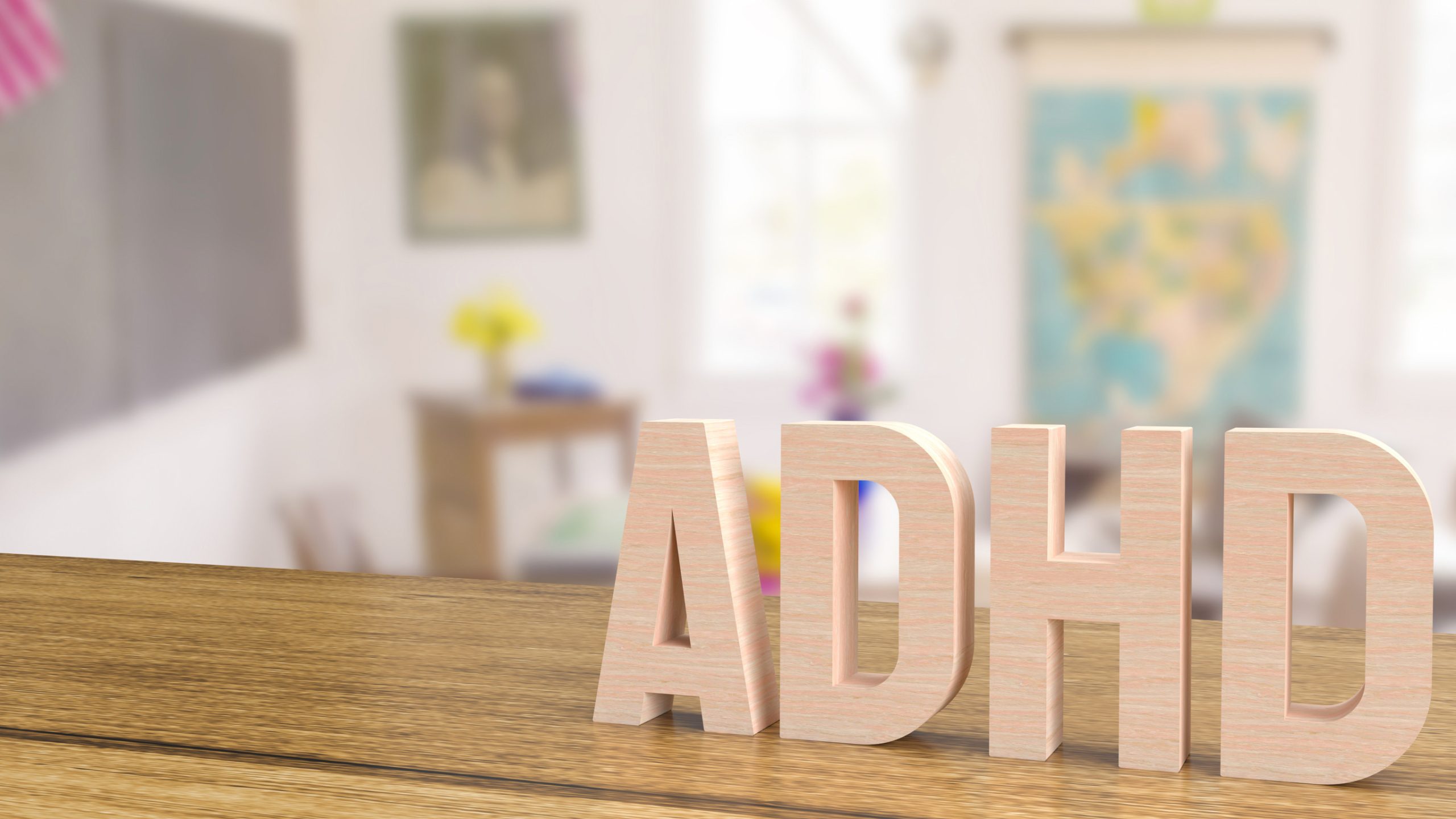 Large wooden letters spelling “ADHD” sit on a classroom desk, with a blurred background featuring a map, blackboard, and decorations—highlighting the importance of ADHD awareness and effective medication management in educational settings.