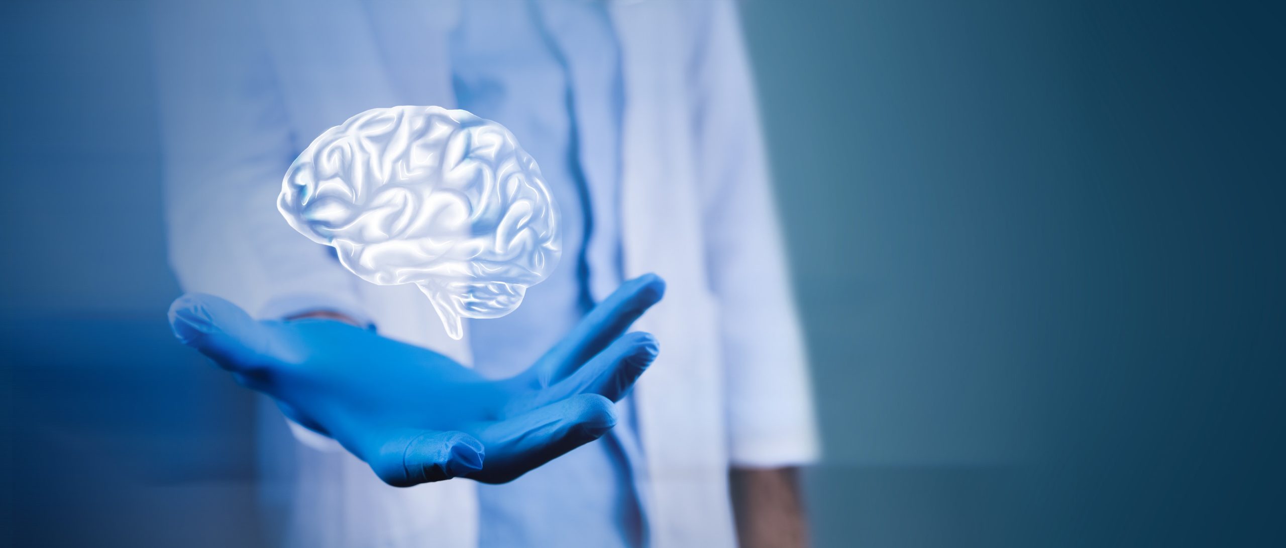 A person in a white lab coat and blue gloves holds out their hand, above which a glowing, holographic image of a brain appears to float against a blue background.