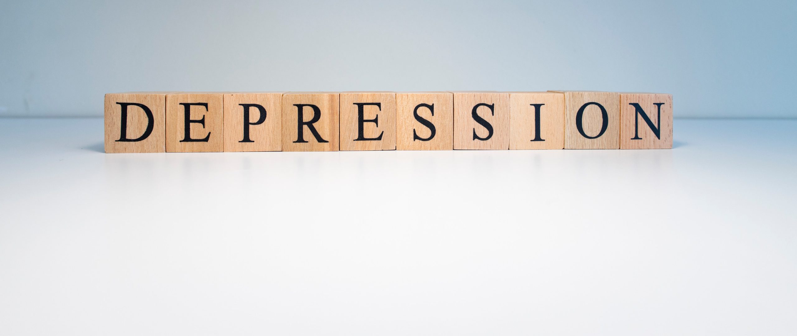 Wooden blocks arranged in a row on a white surface, each block displaying a black capital letter to spell the word "DEPRESSION" against a light background.
