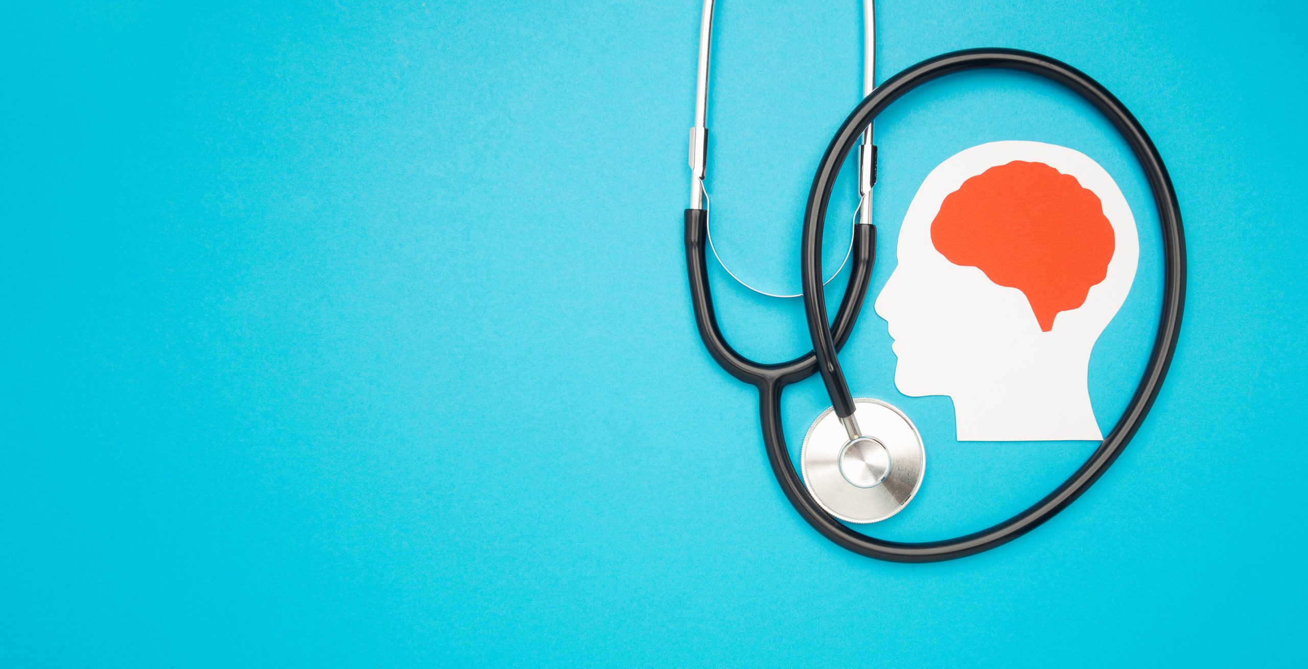 A stethoscope surrounds a white paper cutout of a human head with a red brain on a blue background, symbolizing mental health and healthcare, inspired by Brainerd Lakes Area Psychiatry’s Virtual Calming Room.