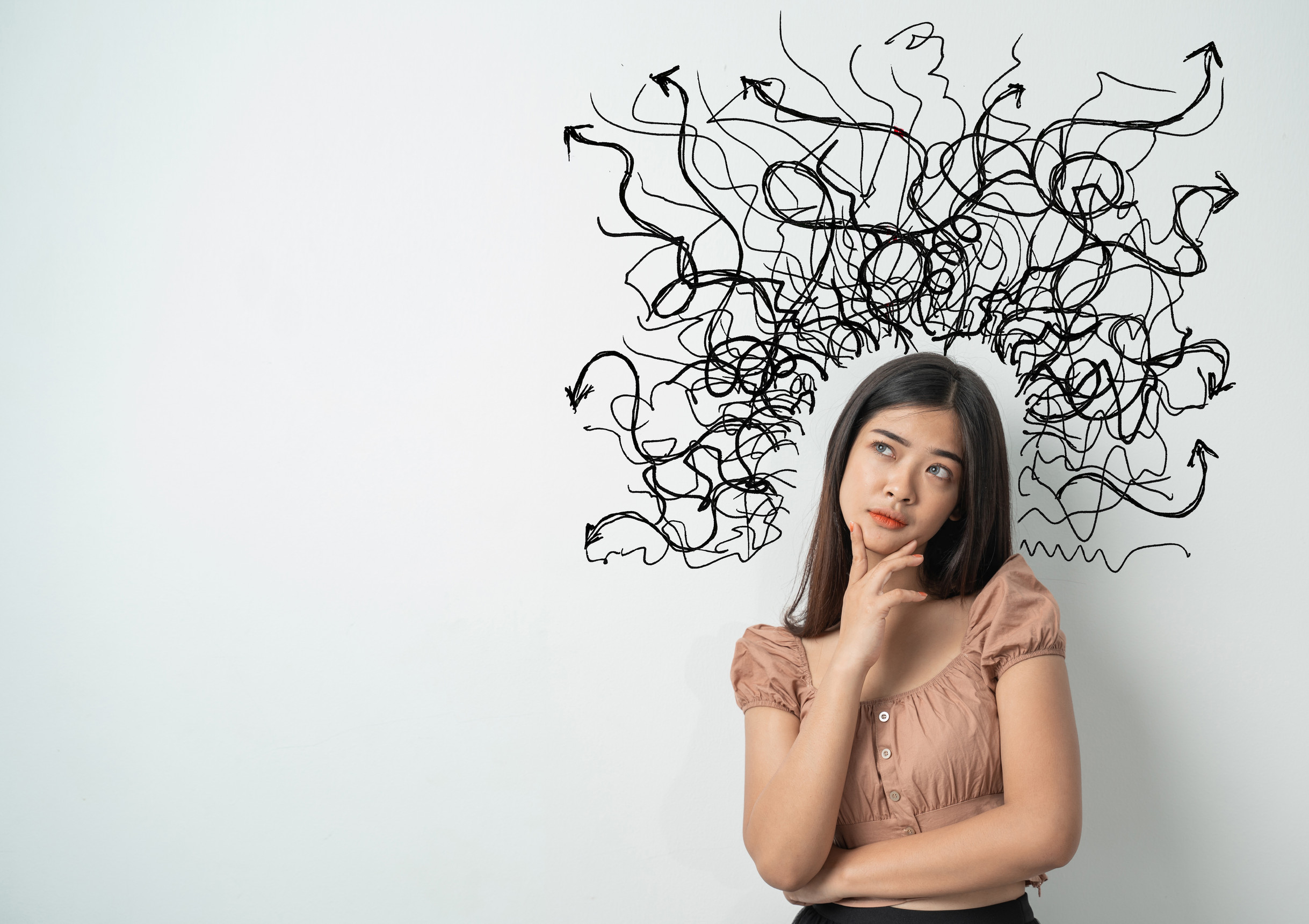 A woman stands thinking with her hand on her chin, looking up. Above her head, chaotic black doodles and arrows suggest confusion or overthinking—reflecting the challenges adults face and highlighting the need for ADHD support from Brainerd Lakes Psychiatry.