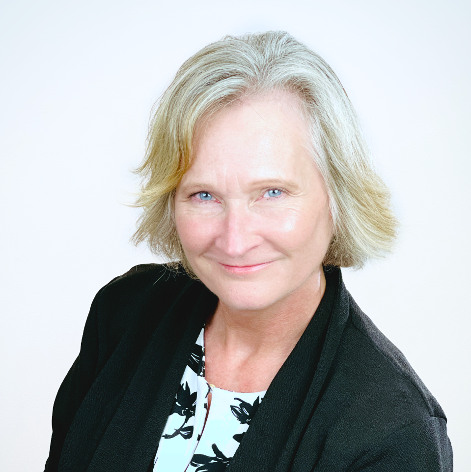 A woman with short blonde hair and blue eyes, one of our trusted providers, smiles gently at the camera. She is wearing a black blazer over a patterned white and black top, posed against a plain light background.