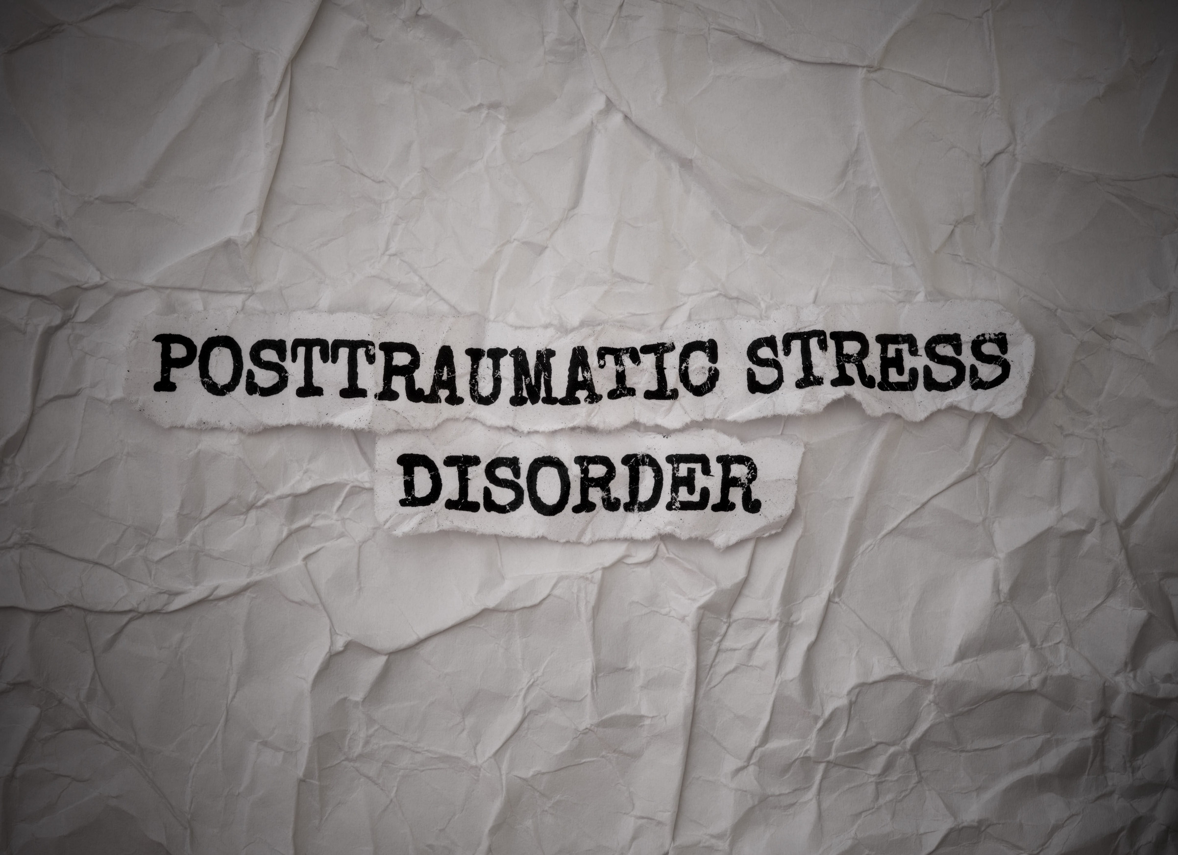 The words “POSTTRAUMATIC STRESS DISORDER” printed on torn paper strips against a crumpled white background, symbolizing the complex brain reactions to trauma triggers.